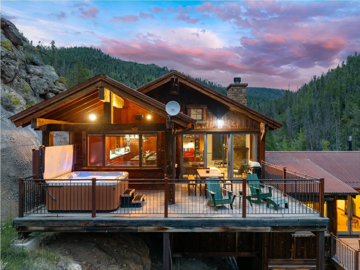 An outdoor deck features a cozy hot tub, ample seating, and a scenic mountain backdrop. The space is ideal for alfresco dining, socializing, and relaxing in the fresh mountain air, perfectly illustrating the direct deck access from the kitchen and dining area.