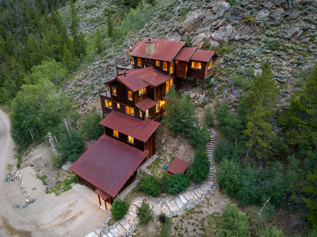 A rustic wooden structure with warm, glowing windows sits nestled in surrounding nature. The outdoor deck offers a vantage point for sunsets and stargazing, inviting guests to relax and socialize amid the dramatic landscape.