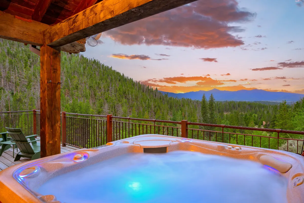 An exterior hot tub set on a deck with panoramic mountain and sunset views. The scene evokes peaceful relaxation, with the hot tub inviting stargazing and soothing soaks beneath the open sky.