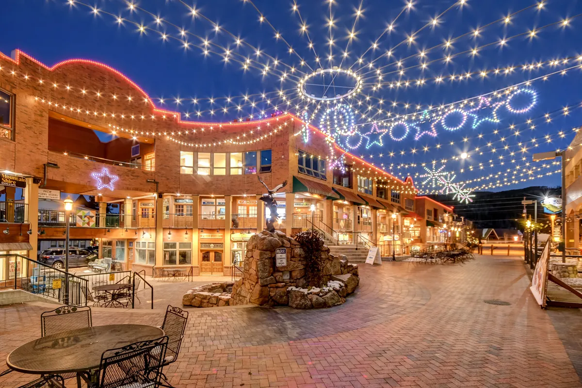 This image captures an outdoor area decorated with twinkling lights, decorative stars, a fountain, and outdoor seating. The festive ambiance suggests gatherings, holiday markets, or evening events, reflecting Winter Park's communal spirit in every season.