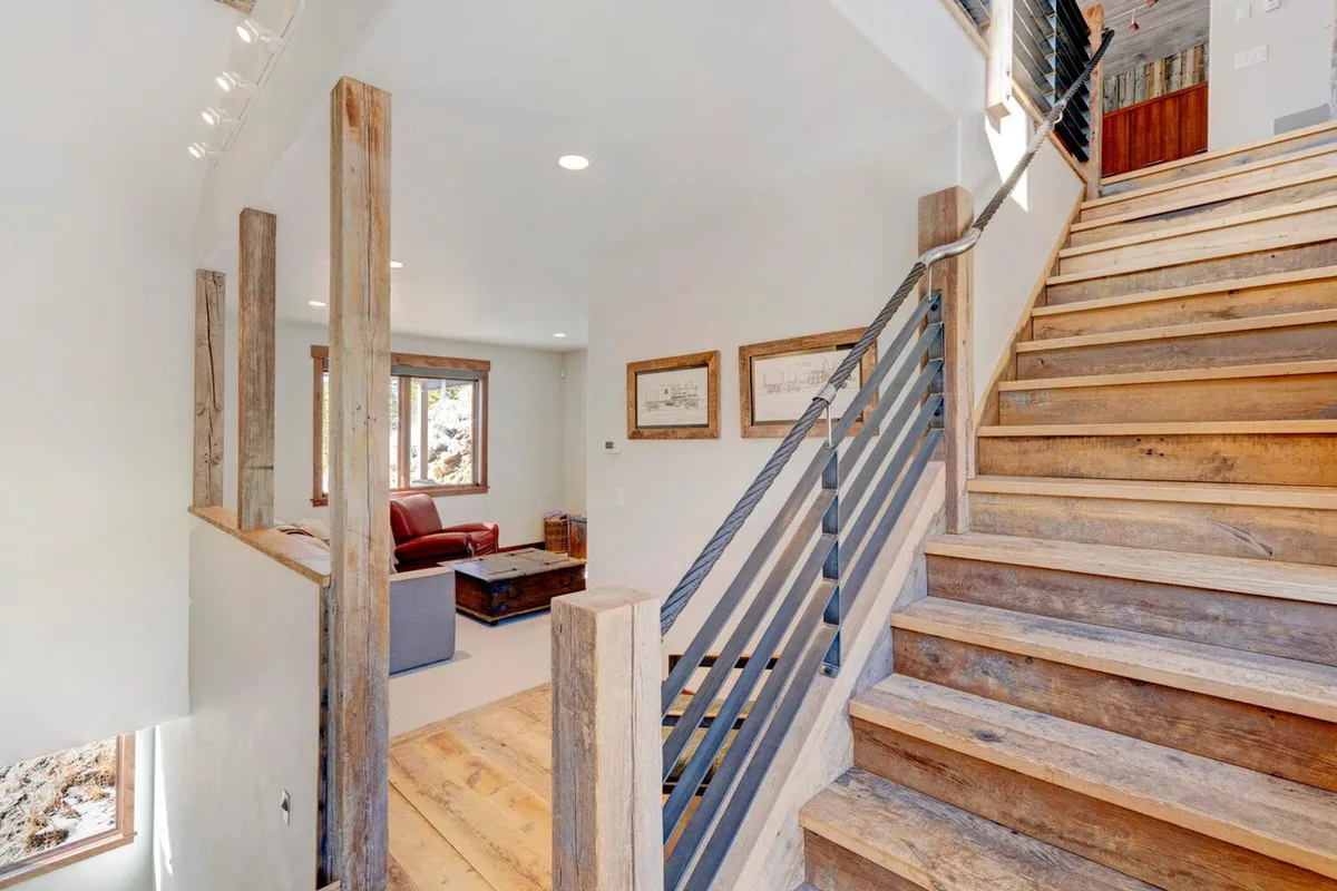 A view of a staircase with elegant wooden railing, adjacent to a cozy seating area next to a window. Natural light enhances the inviting atmosphere, suggesting a seamless flow from entry to main living spaces.