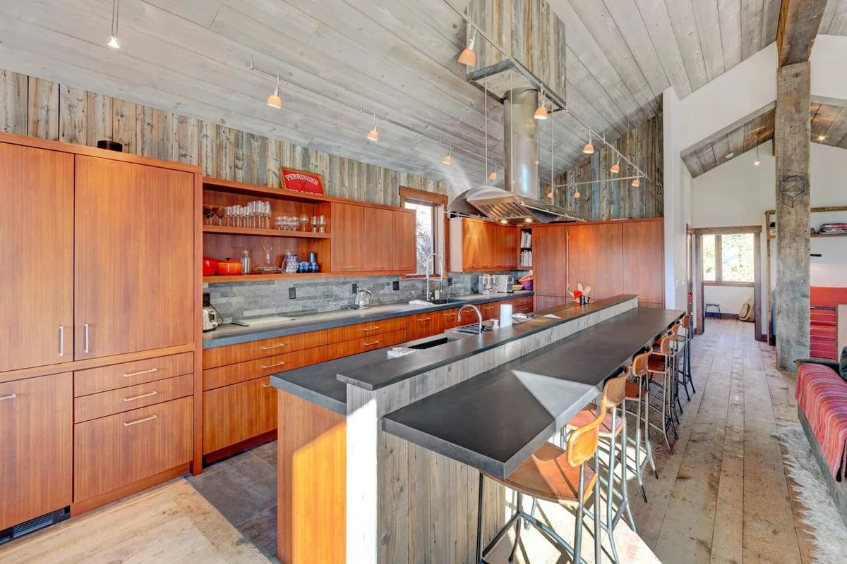 This image showcases a contemporary kitchen with a prominent island, warm wooden cabinetry, sleek stainless steel appliances, and expansive windows that bathe the space in natural light. The setup is perfect for both serious cooking and casual gatherings, echoing a sense of culinary creativity and warmth.